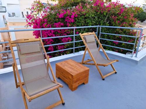two chairs and a wooden box on a balcony with pink flowers at Kykladonisia Traditional Settlement in Fira