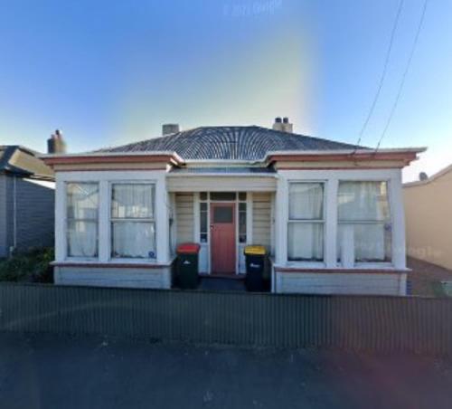 una pequeña casa amarilla con puerta roja en Low Cost Accommodation, en Dunedin