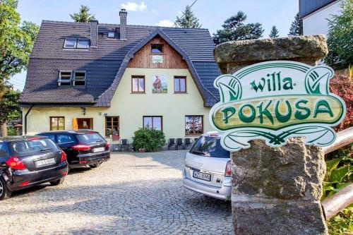 a sign in front of a house with parked cars at Willa Pokusa in Szklarska Poręba