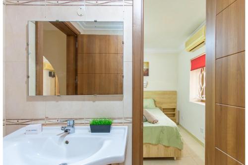 Un baño con lavabo, espejo y cama. en Villa & Pool Apartments in Mellieha Bay, en Mellieħa