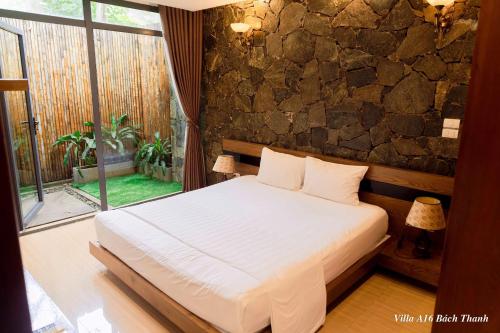 une chambre avec un lit et un mur en pierre dans l'établissement Villa A16 Bách Thanh view hồ - Đại Lải resort, à Phúc Yên
