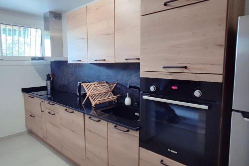 Il comprend une cuisine équipée d'une cuisinière noire et de placards en bois. dans l'établissement Charmant rez de villa, et sa terrasse à Ajaccio, à Ajaccio