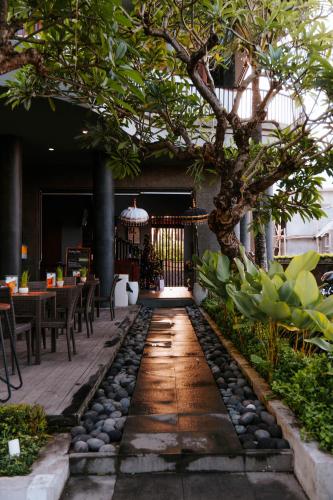 a patio with a tree and a table and chairs at Sense Canggu Beach Hotel in Canggu