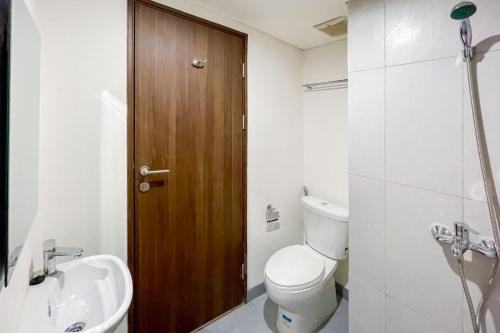 a bathroom with a toilet and a sink and a wooden door at RedLiving Apartemen Royal Park Sentul by Bogor Staycation in Kedungmanggu