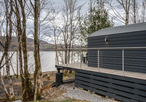 a black building with a deck next to a body of water at Nessie Pod in Fort Augustus