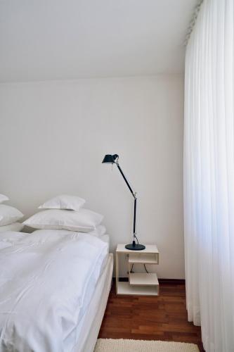 a white bedroom with a bed and a lamp on a night stand at Vier Häuser in Norderney