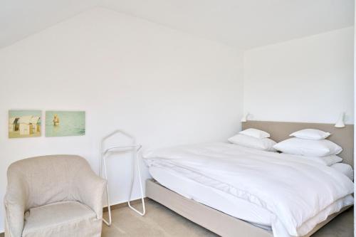 a white bedroom with a bed and a chair at Vier Häuser in Norderney