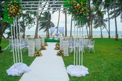 a wedding aisle with white chairs and orange flowers at Cocoa Luxury Resort, Nyali, Mombasa in Mombasa