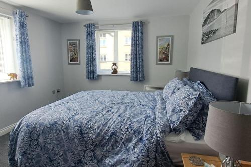 a bedroom with a bed with a blue comforter and two windows at 2 bedroom apartment in Stratford upon Avon with free onsite parking in Stratford-upon-Avon