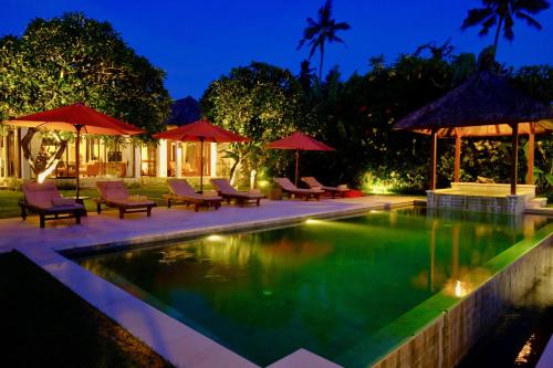 a swimming pool with chairs and umbrellas at night at Villa Kaniksa in Candidasa