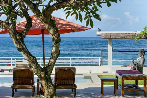 a table and chairs under a tree next to the ocean at Villa Kaniksa in Candidasa