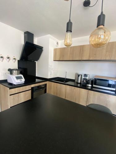 une cuisine avec un comptoir noir et des placards en bois dans l'établissement Capbreton - Appt NEUF - 4 pers - 2 ch, à Capbreton