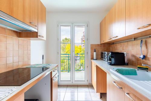 une cuisine avec des placards en bois et une grande fenêtre dans l'établissement GuestReady - Havre de Paix à Courbevoie, à Courbevoie