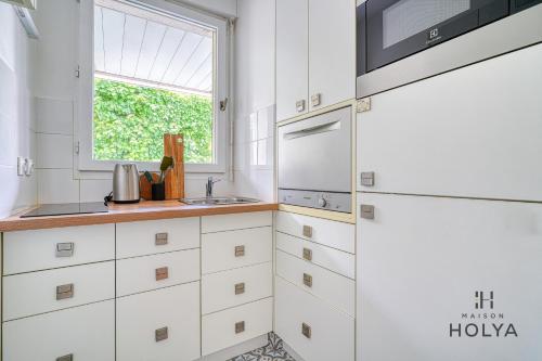 une cuisine avec des armoires blanches et une fenêtre dans l'établissement Le Curieux - À deux pas de Paris - 314B, à Rueil-Malmaison