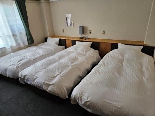 two beds in a hotel room with white sheets at Plaza Inn Kawaguchiko in Fujikawaguchiko