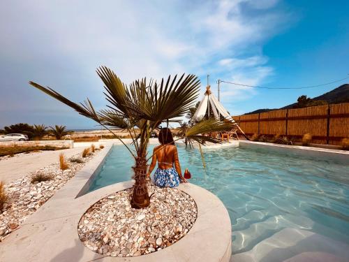 a woman sitting next to a palm tree next to a swimming pool at Amo Golden Suites in Chrysi Ammoudia