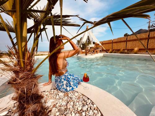 a woman sitting next to a swimming pool at Amo Golden Suites in Chrysi Ammoudia