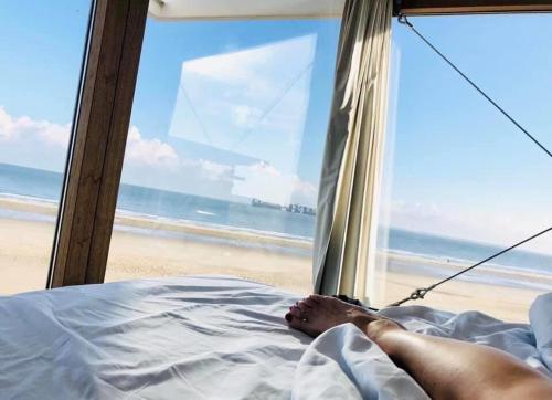 a person laying on a bed in front of the beach at Strandhuis, Beachhouse - Slapen op het strand, Sleep at the beach in Nieuwvliet