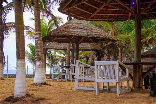 a row of white chairs on a beach with palm trees at Atlantic Bay Resort, Prampram in Prampram