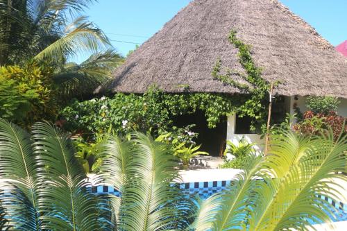 casa atropical com telhado de palha e palmeiras em Aurora Boutique Hotel Jambiani em Jambiani