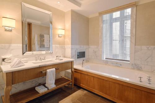a bathroom with a tub and a sink and a mirror at Corinthia London in London