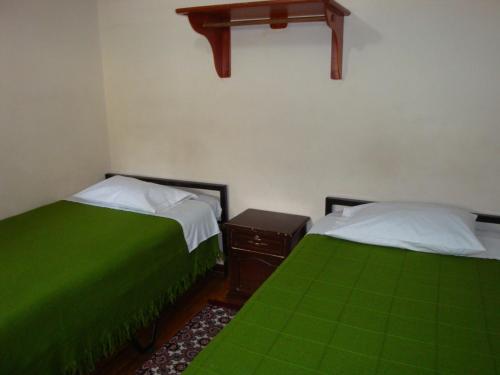 two beds in a room with green sheets at Hostal Santa María Gracia in Quito