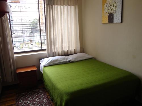 a bedroom with a green bed with a window at Hostal Santa María Gracia in Quito