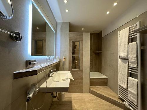 a bathroom with a sink and a tub and a mirror at Köhlers Forsthaus Wellness & Genuss Hotel in Aurich