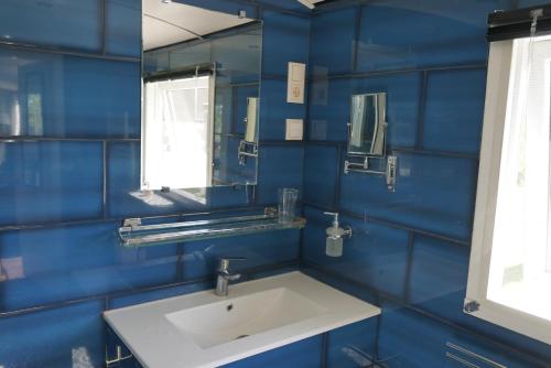 a blue bathroom with a sink and a mirror at Hoeve Zorglust, salonwagen voor 2 personen met extra slaapkamerhuisje voor 2 - 3 kinderen in Koudekerke
