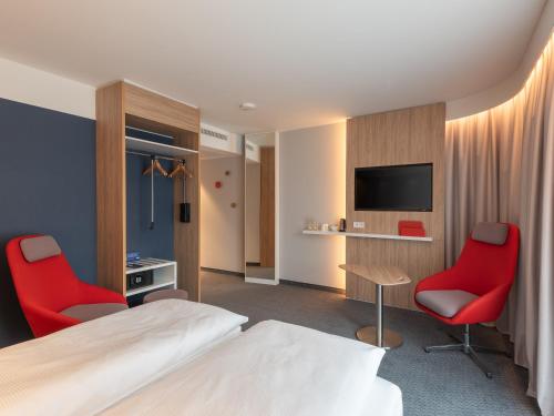 a hotel room with a bed and two red chairs at Holiday Inn Express Heilbronn by IHG in Heilbronn