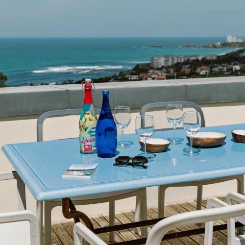 une table bleue avec des verres à vin et des bouteilles sur un balcon dans l'établissement APPARTEMENT PISCINE TERRASSE 1 MIN PLAGE et GOLF, à Bidart