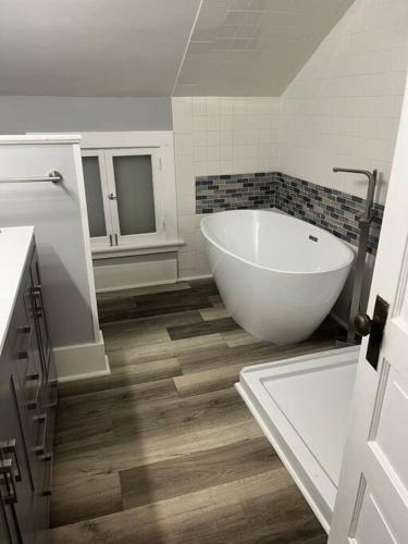 a bathroom with a large white tub and wooden floors at 515Escape - Near downtown, private backyard, firepit, bbq, fun! in Lake Geneva