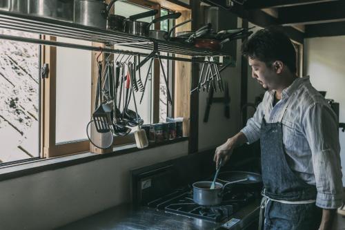 a man stirring a pot on a stove in a kitchen at ruisseau in Ogawa