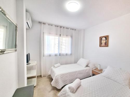 a white bedroom with two beds and a window at Apartamento con piscina, urbanización privada by AlohaPalma in Águilas