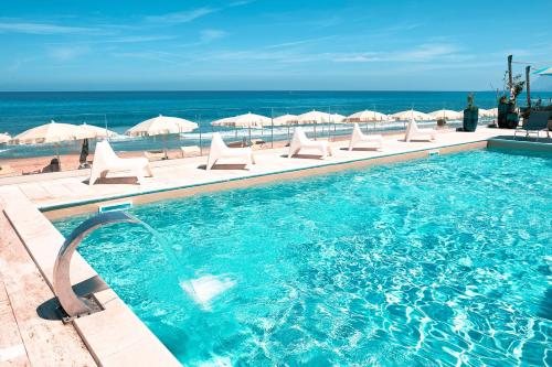 a swimming pool with chairs and umbrellas and the ocean at Hotel La Battigia in Alcamo Marina