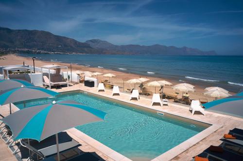 a swimming pool next to a beach with umbrellas at Hotel La Battigia in Alcamo Marina