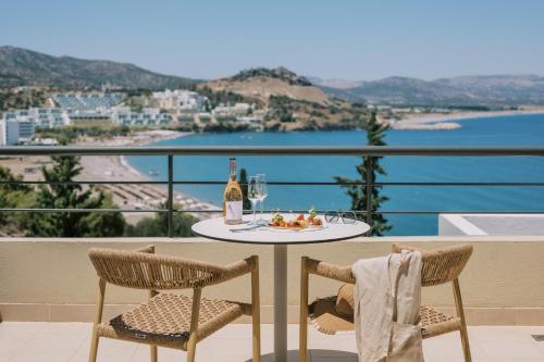 a table with a bottle of wine and a plate of food on a balcony at Lindos Mare, Seaside Hotel in Líndos