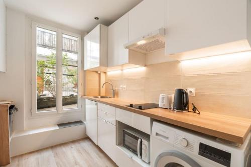 une cuisine avec des armoires blanches, un évier et une fenêtre dans l'établissement Appartement cosy canal Saint Martin, à Paris