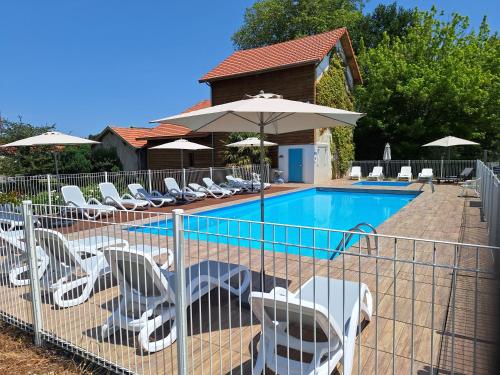 une clôture avec des chaises et une piscine avec des parasols dans l'établissement Mobil home - Domaine du Vieux Moulin, à Saint-Julien-en-Born