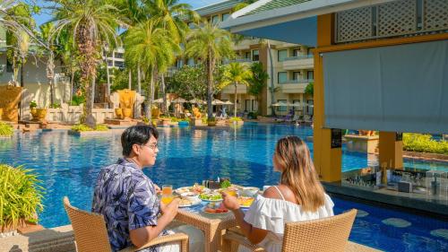 芭东海滩Holiday Inn Resort Phuket, an IHG Hotel的坐在游泳池前桌边的男人和女人