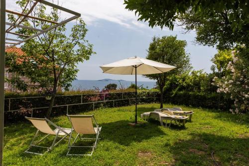 eine Gruppe Stühle und ein Regenschirm im Gras in der Unterkunft Apartments Villa Mare in Mlini
