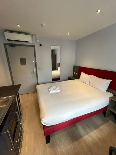 a bedroom with a large white bed with a red headboard at London Walthamstow Hotel in London