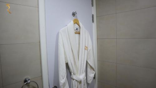 a white robe hanging on a door in a bathroom at Dainty 1BR Apartment in Masdar - Cozy Stay Near Masdar Park & City Centre in Abu Dhabi