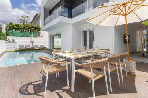 a dining table with chairs and an umbrella next to a swimming pool at Casa John Lisboa-Piscine chauffée en option in Charneca