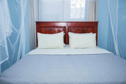 a bed with a wooden headboard and two white pillows at Occazia Hotel in Mbarara