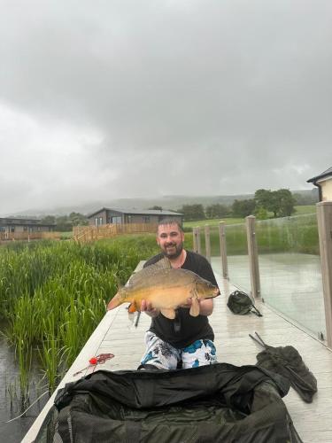 a man sitting on a dock holding a fish at Luxurious and Peaceful Lakeside House, Clitheroe in Clitheroe