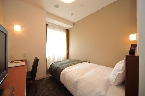 a hotel room with a bed and a window at Dormy Inn Tomakomai in Tomakomai