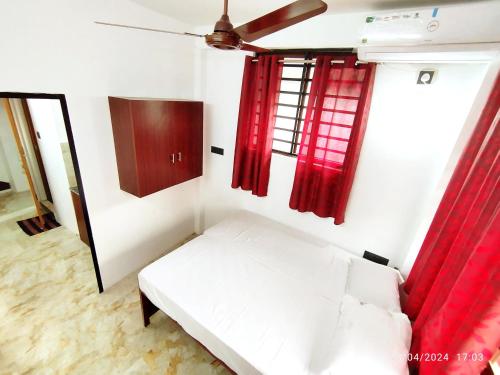 a small room with a white bed and red curtains at Pleasant Homes in Ernakulam