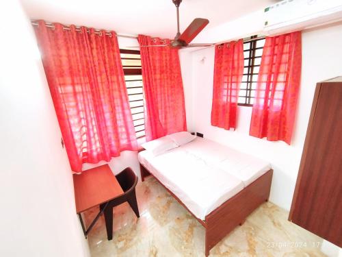 a small bedroom with red curtains and a bed and a chair at Pleasant Homes in Ernakulam