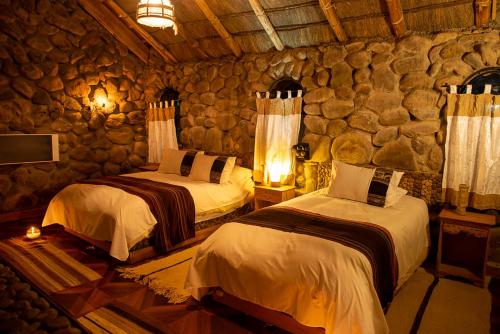 a bedroom with two beds and a stone wall at Tambo Coquesa Lodge in Coquesa